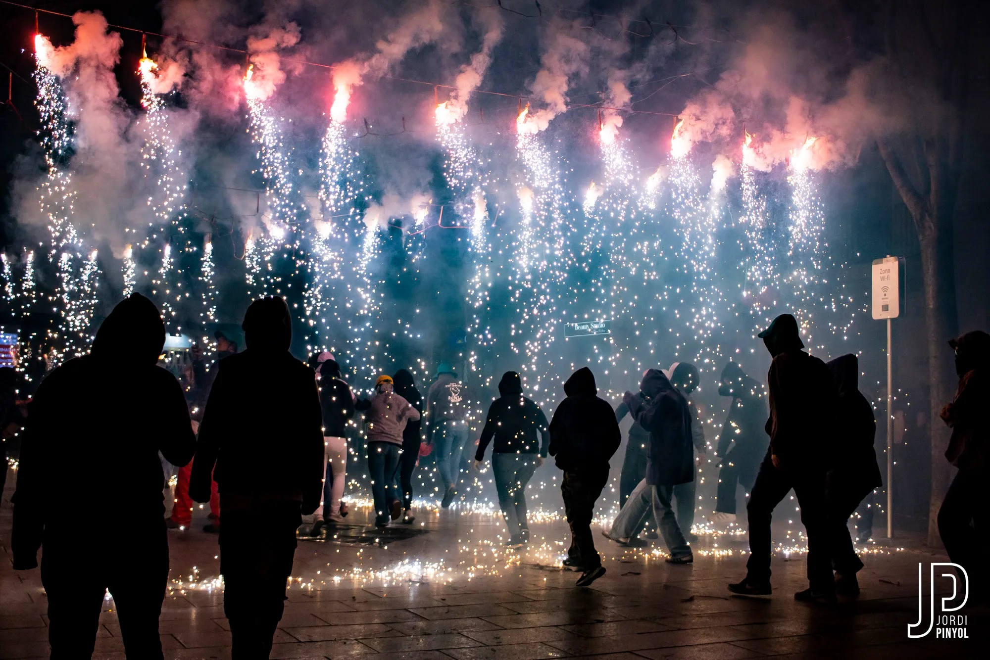Pluja de guspires blanques sobre els diables en un carrer estret durant el correfoc