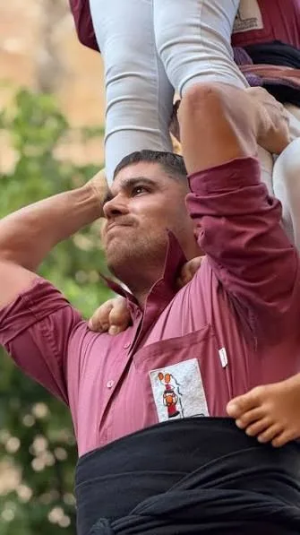 Un casteller amb la camisa granat dels Castellers d’Esparreguera aguantant el pes del castell
